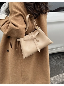 Detail of minimalist beige trapezoid bucket bag with decorative bow on stylish model