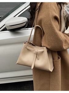 Chic beige leather bucket bag with knot detail worn with a wool coat in urban street setting