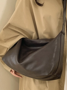 Minimalist dark brown leather tote bag with wide shoulder strap worn by a model