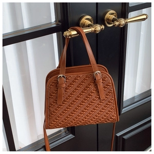 Gros plan d'un sac tressé marron caramel avec boucles métalliques sur une porte sombre