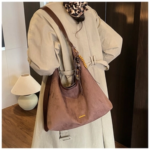 Détail d'un sac hobo en daim marron avec des perles en bois et des franges sur le côté