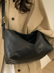 Minimalist black large capacity leather tote bag with gold buckle on beige trench coat