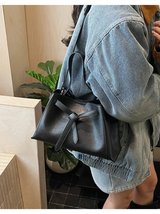Detail of minimalist black leather bucket bag with decorative tie-knot and trapezoidal shape