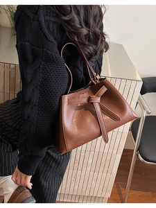 Brown leather bucket bag with knot detail worn by a model in a modern interior setting