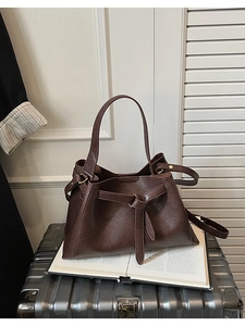 Detail view of coffee brown bucket bag with knotted belt design on an aluminum suitcase