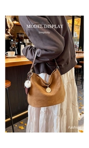 Brown PU leather shoulder bag with white pompom charm in a cozy cafe setting