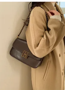 Gros plan d'un sac bandoulière vintage marron foncé avec boucle dorée sur un manteau
