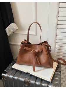 Detail shot of brown lychee grain leather bucket bag with decorative belt knot on silver luggage
