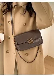 Détail d'un sac bandoulière marron foncé avec boucle géométrique en métal doré chic