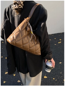 Macro view of a brown quilted tote bag with woven tassels worn on the shoulder outdoors
