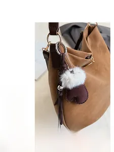 Detail of brown faux fur mitten charm hanging on a vintage texture leather tote bag