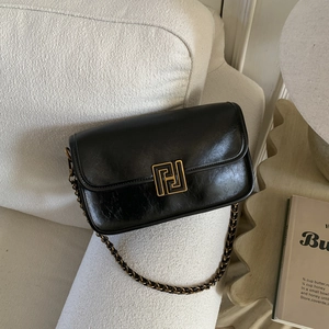 Détail d'un sac bandoulière en cuir noir avec fermoir doré et chaîne en métal sur sofa