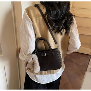 Vue détaillée d'un sac à main en daim marron foncé avec un charm lapin en peluche et bandoulière