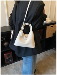 Detail shot of cream-colored lychee textured bucket bag with metal twist lock and shoulder strap
