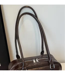 Detailed close-up of dark brown glossy leather underarm bag with silver dual zippers