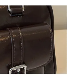 Detail of dark brown polished leather shoulder bag featuring silver buckle and fine stitching