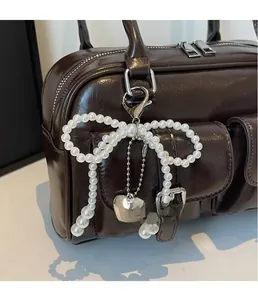 Detail of pearl bow charm with silver heart pendant on a vintage bowling shoulder bag