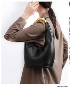 Detail of minimalist black leather underarm bag with sleek gold metallic handle on model