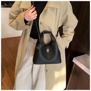 Detail of black pebbled leather bucket bag with silver twist lock on model's outfit