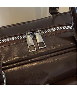 Detail of silver smooth metal zippers on dark brown wax-textured leather bag