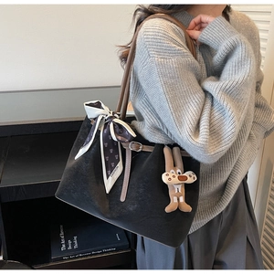 Detail of black tote bag with brown handles, fashion scarf and plush rabbit charm