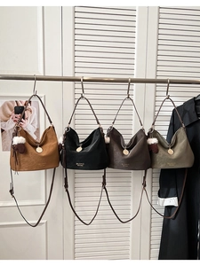 Four textured crossbody bags in brown, black, coffee, and green with plush ball charms