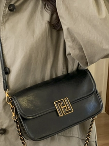 Sac bandoulière rétro en cuir noir avec fermoir doré en H porté par un mannequin