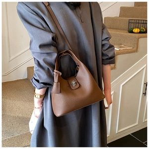 Detail of a dark brown pebble leather bucket bag with silver lock on a gray dress