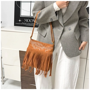 Detail of brown suede crossbody bag featuring bohemian white embroidery and long fringe tassels