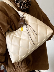 Quilted cream tote bag with heart charm and tassel detail worn by model on shoulder