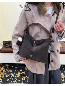 Detail of dark brown suede shoulder bag with niche design logo and plush keychain