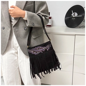 Detailed view of bohemian floral embroidery and long fringes on a black suede shoulder bag