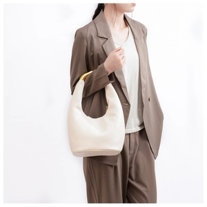 Detailed macro view of a cream leather bag featuring a sculptural gold metal handle