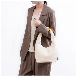 Detailed view of cream leather hobo bag featuring elegant gold metal handle accent on a model