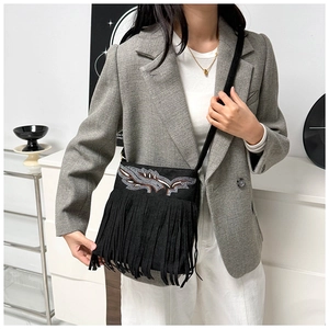 Detail of bohemian black crossbody bag featuring intricate embroidery and long tassels on a model