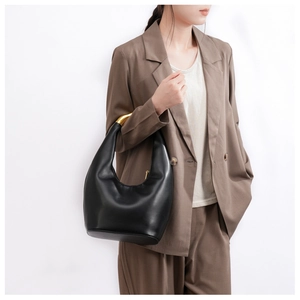Detail view of black leather handbag featuring a unique gold metal curved handle on the side