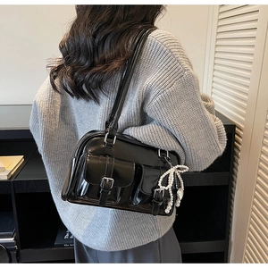 Detail of black glossy faux leather shoulder bag with decorative pearl bow charm and buckle