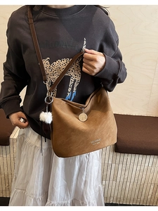 Close-up of brown textured crossbody bag with a plush ball and metal charm detail