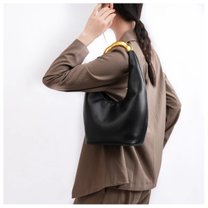 Minimalist black leather underarm bag with asymmetric gold metal handle shown on model