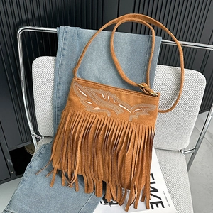 Close-up of brown suede crossbody bag with boho embroidery and long fringe on a white chair