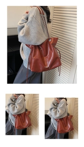 Detail view of the rust red drawstring bucket bag with a metal chain shoulder strap