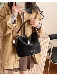 Detail of black matte shoulder bag featuring brown leather strap and gold metal charm