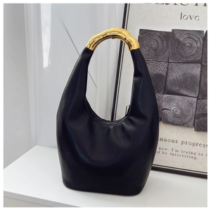 Close-up of sleek black leather bag featuring an asymmetric gold metallic handle detail