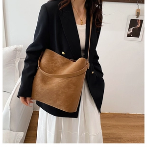 Ampia borsa a secchiello marrone in pelle opaca abbinata a un look formale da ufficio