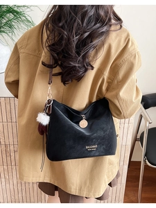 Black matte tote bag detail with golden metal pendant and white fuzzy pompom charm