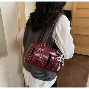 Detail of burgundy glossy faux leather shoulder bag with pockets and pearl bow charm