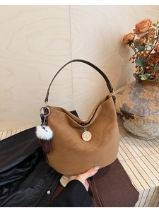 Detail of brown suede bucket bag featuring golden circular pendant and soft white pompom