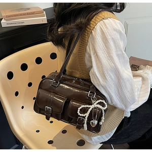 Detail view of brown patent leather shoulder bag with side pearl bow charm and twin pockets