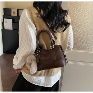 Detail of dark brown vintage crossbody bag with woven pattern and plush rabbit charm