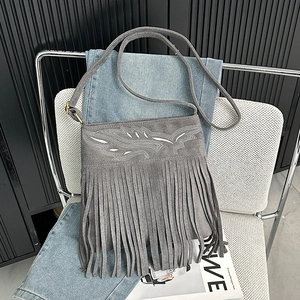 Detail of grey suede crossbody bag with vintage embroidery and long fringe tassels